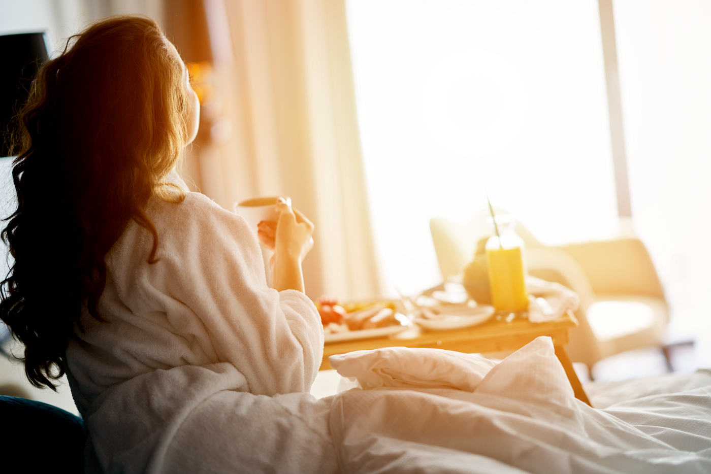 Vrouw drinkt koffie in hotelkamer met ochtendzon