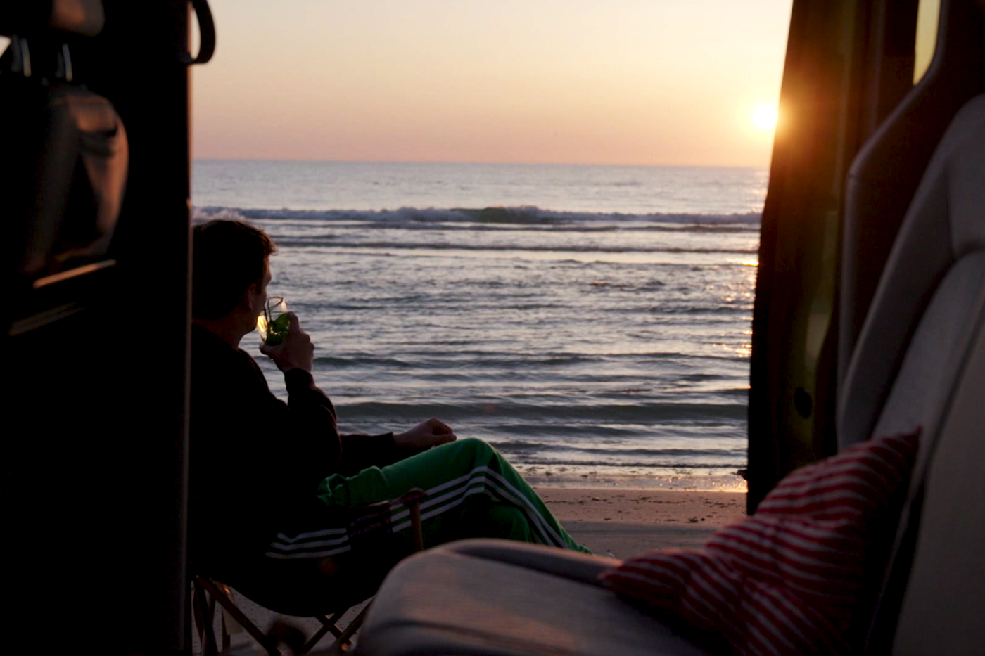 Jurre parkeert zijn elektrische auto op het strand, drinkt wat en kijkt uit over de zee naar de zonsondergang